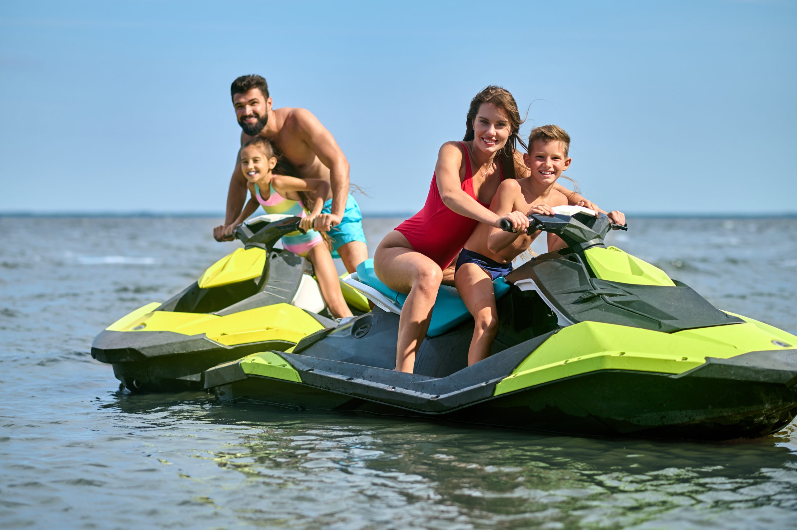 Father, mother, daughter and son racing on jet-skis enjoying watercraft in ocean, active summertime.