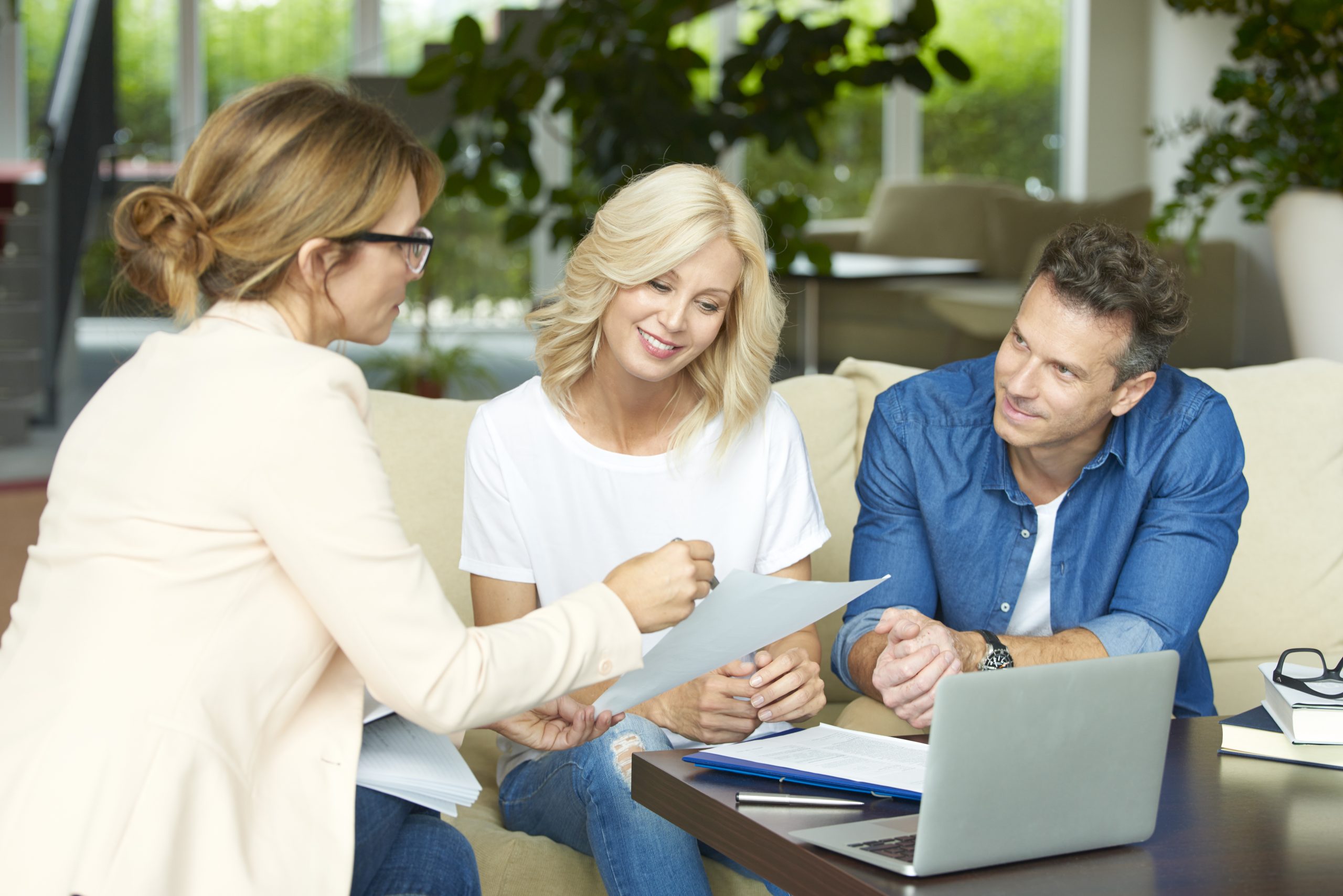 Shot of a middle aged couple consulting with real estate agent in their home while sitting on sofa.